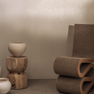 Designinterieur met metallic Platre Lin RM 617 91 behang, houten bijzettafel en modern golvend stoelontwerp.