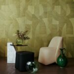 Modern interieur met een geometrisch groen behang (Puzzle3-3019-2), een crèmekleurige stoel, zwarte en marmeren bijzettafels en groene glazen decoratieobjecten.