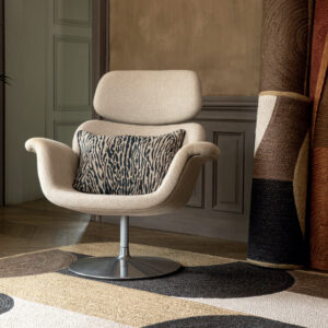 Beige designstoel met metalen voet, voorzien van een sierkussen met dierlijk patroon, in een stijlvol interieur met opgerolde vloerkleden.