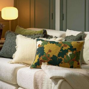 Sfeervolle zithoek met het sierkussen Jane CO-253-67-02 met bloemendessin op een bank met gedrapeerde plaids en andere kussens.