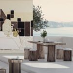 Stijlvol terras met houten eettafel, kunstmuur van Elitis en uitzicht op zee en bergen.