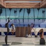 Moderne lobbyruimte met kunstobjecten en een kleurrijke muurdecoratie van palmbomen en mensen aan zee.