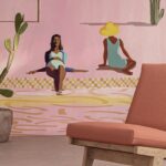 Interieur met oranje loungestoel, grote kamerplanten en een muurschildering van relaxende vrouwen bij een zwembad.