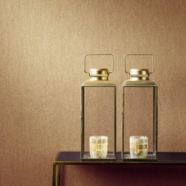 Twee glazen lantaarns met goudkleurige accenten en kaarsen erin staan op een tafel voor een beige wandbekleding uit de collectie Les Unis 6 van MVIC.