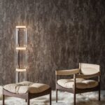 Designinterieur met een Stucco3-AYDW-2 muur, moderne glazen vloerlamp en een houten loungestoel met bijpassende hocker op een zacht vloerkleed.