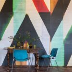 Houten eettafel met blauwe stoelen en bloemen in vazen, voor een kleurrijk geometrisch wandontwerp genaamd Sunbeams.