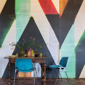 Houten eettafel met blauwe stoelen en bloemen in vazen, voor een kleurrijk geometrisch wandontwerp genaamd Sunbeams.