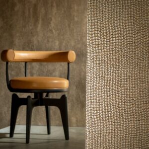Een designstoel met leren zitting en rugleuning staat naast een wand bekleed met het goudkleurige mozaïekpatroon Tessera2-GXAI-3.