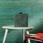 Moderne interieursetting met groen-blauw VP-712-05 behang, een witte tafel, decoratief beeld en rode stoel met boeken.