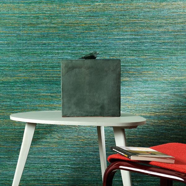 Moderne interieursetting met groen-blauw VP-712-05 behang, een witte tafel, decoratief beeld en rode stoel met boeken.