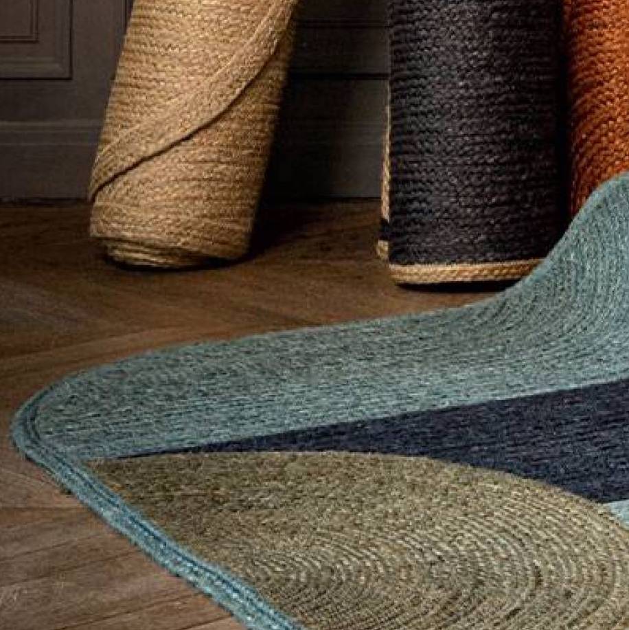 Gevlochten kleurrijk kleed Acapulco met opgerolde juten tapijten op houten vloer.