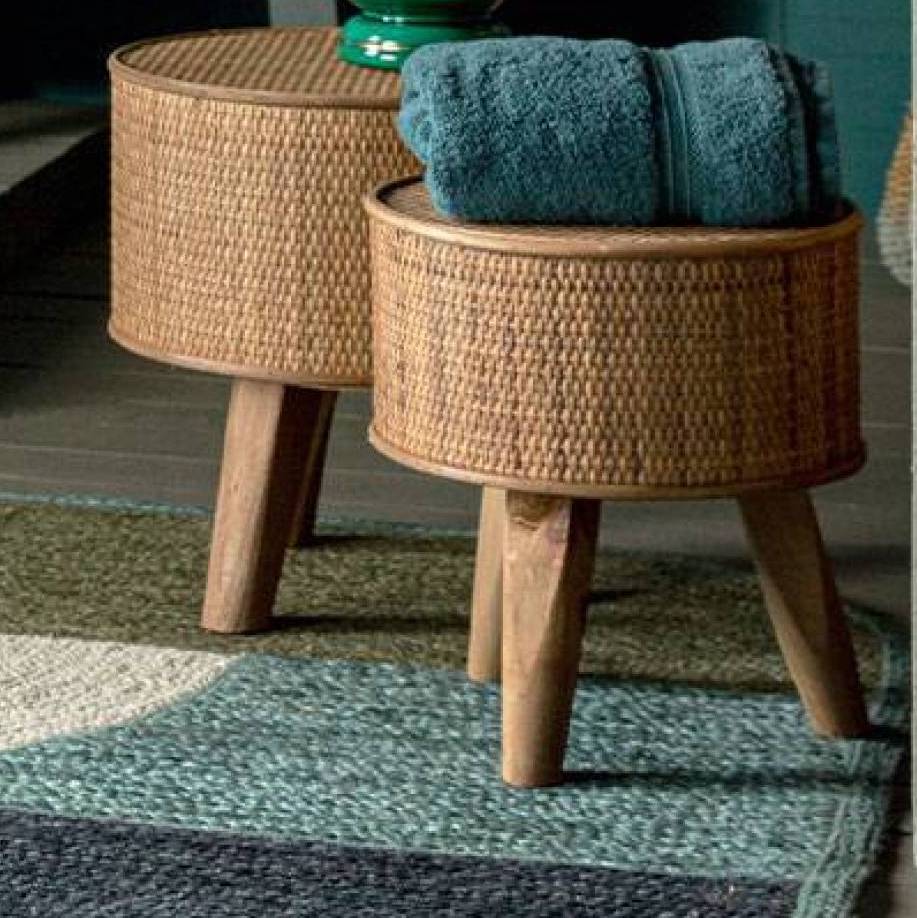 Twee ronde rotan bijzettafeltjes met houten poten, waarvan één is gedecoreerd met een opgerolde blauwe handdoek.