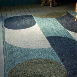 Geweven vloerkleed Acapulco met abstract patroon in blauwe, groene en crèmekleuren op houten vloer.