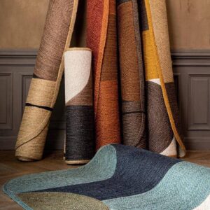 Verschillende kleurrijke Acapulco-vloerkleden van gevlochten materiaal staan opgerold tegen een muur, met één kleed gedeeltelijk uitgespreid op de vloer.