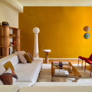 Modern ingerichte woonkamer met een okergele accentmuur, witte loungebank, houten meubels en stijlvolle decoratie.