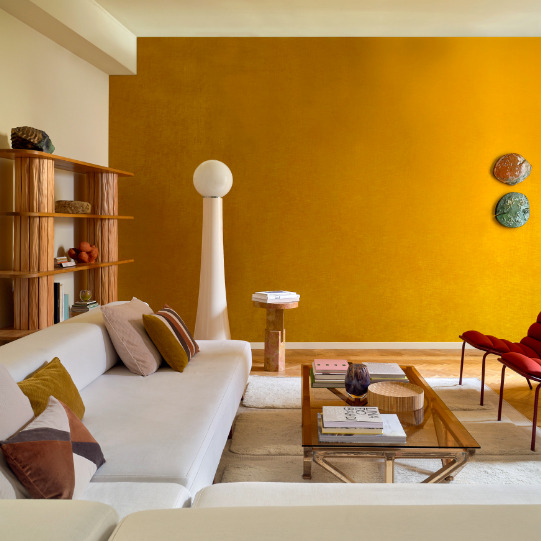 Modern ingerichte woonkamer met een okergele accentmuur, witte loungebank, houten meubels en stijlvolle decoratie.