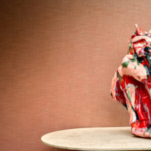 Abstract beeldhouwwerk in rood- en groentinten op een ronde tafel tegen een roze textuurmuur met Alcove RM 410-51 behang.
