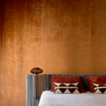 Sfeervolle slaapkamer met Alcove 2 RM 410-70 fluwelen wandbekleding, een gestreept hoofdbord en decoratieve kussens.