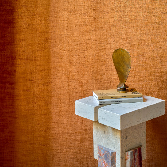 Decoratief stilleven met boeken en sculptuur op een marmeren zuil, voor een warmoranje Alcove 2 RM 410-70 gordijn.