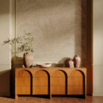 Houten dressoir met keramische vazen en een tak voor een wand met beige Arte Lanai Maui 81530 behang met palmbladpatroon.