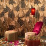 Interieur met Arte Pavartina 97562 behang in bruin- en goudtinten, een sierlijke fauteuil met franjes, poef en rode lamp.