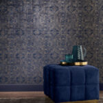 Donkerblauw Casamance Jali behang met goudkleurig patroon achter een fluwelen poef met dienblad en glazen.