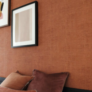 Detail van een interieur met Casamance Johara behang in warme roestkleur, sierkussens en moderne wanddecoratie.