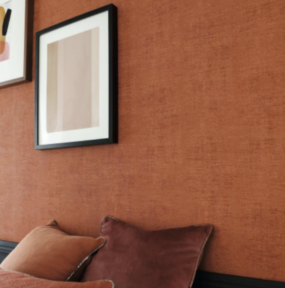 Detail van een interieur met Casamance Johara behang in warme roestkleur, sierkussens en moderne wanddecoratie.