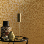 Modern interieur met Casamance Tiznit behang in goudtinten en decoratieve objecten op een zwarte bijzettafel.
