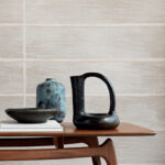 Keramische decorstukken op een houten tafel voor een muur met het textielbehang Caravane Moshi Moshi VP 942 01.