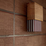 Wandlamp Moshi Moshi van Caravane met gevlochten kap en gestreepte stof tegen een bruinrood textuurbehang.