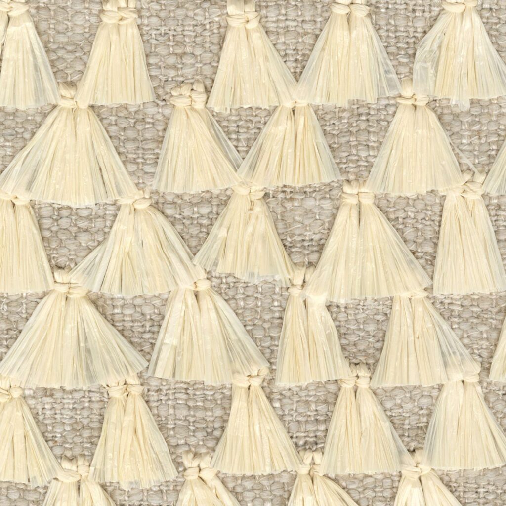 Detail van de Elitis Baleares Finca LZ 897 04 stof met beige raffia kwastjes op een grof geweven ondergrond.