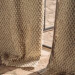Close-up van Elitis Baleares Finca LZ 897 04 gordijnstof met een reliëfstructuur van beige driehoekige patronen in zonlicht.