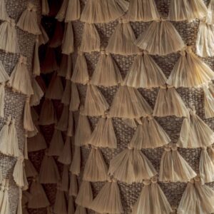 Detail van Elitis Baleares Finca LZ 897 04 stof met textuur van geweven linnen en decoratieve beige franjes.
