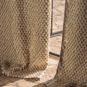 Close-up van Elitis Baleares Finca LZ 897 04 gordijnstof met een reliëfstructuur van beige driehoekige patronen in zonlicht.