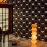 Sfeervolle interieurhoek met Elitis Hanji Toshima RM 1061 75 behang in donkere tinten en een golvende staande rieten lamp.