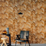 Modern interieur met Elitis Sauvages VP 968 22 behang in warme houttint met visgraatpatroon, zwarte stoel en bijzettafels.
