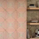 Decoratief wandpaneel uit de Elitis Cordes Sensibles-collectie met geometrisch patroon in roze- en natuurtinten naast een houten plank met boeken en woonaccessoires.