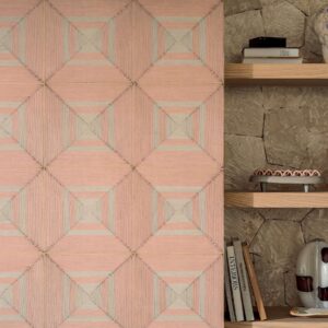Decoratief wandpaneel uit de Elitis Cordes Sensibles-collectie met geometrisch patroon in roze- en natuurtinten naast een houten plank met boeken en woonaccessoires.