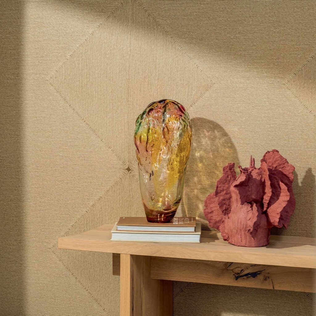 Decoratieve opstelling met een glazen vaas en terracotta kunstobject op een houten tafel voor een Elitis Cordes Sensibles wandbekleding.