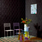 Moderne interieursetting met Elitis Forms Mone Chenille wandbekleding, twee designstoelen, een kleurrijk vloerkleed en een glazen bijzettafel met bloemenvaas.