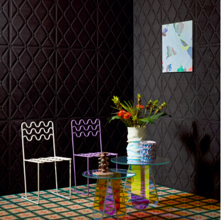 Moderne interieursetting met Elitis Forms Mone Chenille wandbekleding, twee designstoelen, een kleurrijk vloerkleed en een glazen bijzettafel met bloemenvaas.