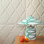 Decoratieve tafellamp met groen-wit patroon op een houten oppervlak tegen een gewatteerd Elitis Forms Mone Lin behang.