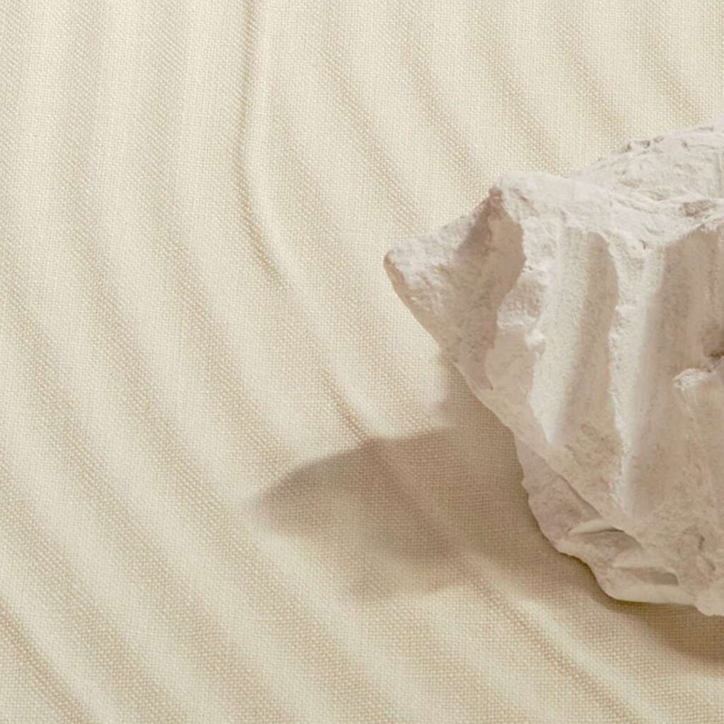 Grote witte steen op beige Elitis Le Jardin d’Aloès Palimpseste linnen stof met subtiel golvend reliëf.