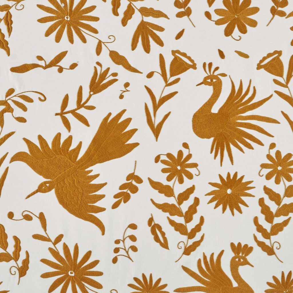 Okergele Elitis-stof Comala LZ 891 22 met geborduurde bloemen en vogels op een witte achtergrond.