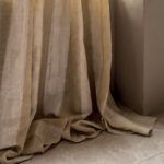 Beige Elitis Ephemere Univers LI 895 02 stofgordijn in linnenlook, elegant vallend op een stenen vloer.