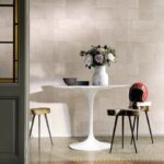 Moderne interieursetting met Elitis Indomptee Appaloosa VP 618 07 behang, ronde witte tafel, bloemenvaas en designkrukken.