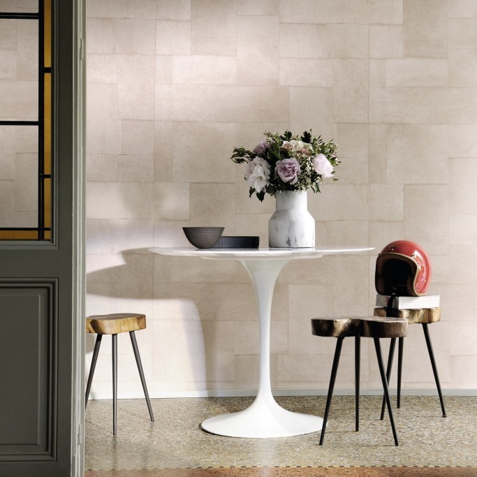 Moderne interieursetting met Elitis Indomptee Appaloosa VP 618 07 behang, ronde witte tafel, bloemenvaas en designkrukken.