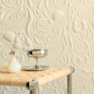 Decoratieve wand met het reliëfpatroon 'Le Jardin d’Aloès' in beige linnenlook, met een metalen tafeltje waarop een zilverkleurige schaal en een glanzend peervormig object staan.