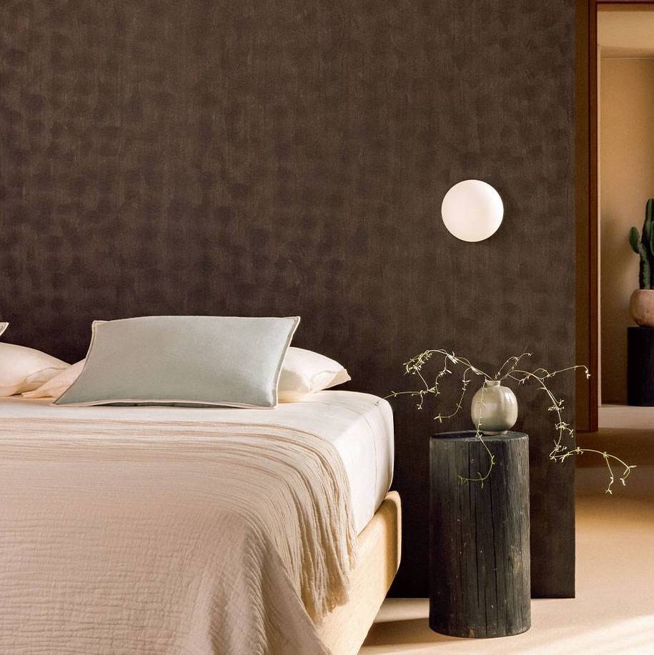 Moderne slaapkamer met een sculpturaal donkerhouten muurpaneel, minimalistische verlichting en een stijlvol nachtkastje met vaas.